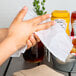 A person using a 8" x 10" lemon scented moist towelette to wipe their hands at a table in a restaurant.