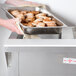 A person holding a tray of food in a school kitchen using an Advance Tabco electric hot food table.