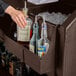 A person pouring liquor from a clear bottle into a glass on a Cambro dark brown portable bar.