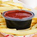 A clear oval plastic lid on a container of ketchup on french fries.