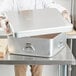 A person holding a Vollrath aluminum roasting pan with handles.
