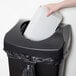 A hand putting a white box into a Rubbermaid black square commercial trash can.