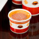 Two Choice paper soup containers with plastic lids on a table.