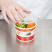 A hand putting vegetables in a Choice paper soup container with a plastic lid.