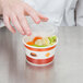 A hand reaching for a plastic lid on a container of vegetables.