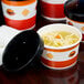 A table with several black and white Choice paper soup containers filled with soup, one with noodles.