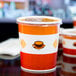 A white paper soup container with orange and white stripes and a vented plastic lid.