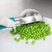 A person in gloves uses a Vollrath teal metal scoop to pick peas.