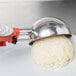 A hand using a Vollrath orange squeeze disher to serve rice.