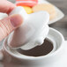 A person's hand holding a white Tuxton china teapot lid.