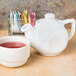 A white Tuxton china teapot and a cup of tea.