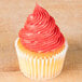 A cupcake with pink French star piped frosting on a wooden table.