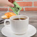 A hand pouring Regal Natural Stevia into a white cup of tea.