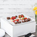 A white square porcelain plate with a liner holding chocolate covered strawberries and chocolate balls.