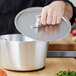 A person using a Vollrath Wear-Ever aluminum pot cover on a silver pot.