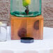 A Cal-Mil glass beverage dispenser filled with water and lemon on a wooden table.