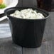 A black oval plastic souffle container with a clear lid.