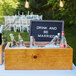 A wooden Cal-Mil ice box on a table with bottles of soda and a sign.