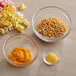 A bowl of corn kernels and a bowl of yellow liquid on a table with bowls of popcorn and butter.