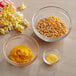 A table with bowls of corn, yellow powder, and yellow paste next to bowls of corn kernels, popcorn, and yellow butter.