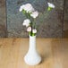 A white Cambro bud vase with pink flowers on a table.