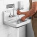 A man using a Regency wall mounted hand sink to wash his hands.