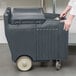 A person pushing a large grey container.