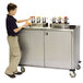 A young boy standing next to a Lakeside stainless steel condiment cart.