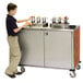 A young boy stands next to a Lakeside stainless steel condiment cart.