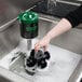 A hand using a Noble Products glass washer brush to clean a glass in a sink.