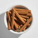 A white bowl filled with several whole cinnamon sticks.