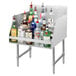 An Advance Tabco stainless steel liquor display rack on a counter with bottles of liquor on it.