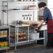 A woman in a chef's uniform using a Regency stainless steel double deck overshelf on a counter in a school kitchen.