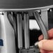 A close-up view of a hand adjusting the tension springs inside a stainless steel heated plate dispenser.