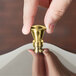 A hand pressing the brass knob of a Vollrath beverage dispenser.