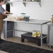 A woman in a professional kitchen standing in front of a Regency stainless steel work table.