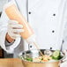 A chef using a Tablecraft INVERTAtop squeeze bottle to pour sauce into a bowl of food.