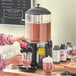 A woman using an Avantco hot beverage dispenser to pour hot chocolate into a glass.