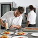 A man in a white shirt using a grater to grate cheese over a plate of food in a room with a Convotherm Maxx Pro Combi Oven.