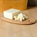 An American Metalcraft oval olive wood serving board with a block of butter on it.