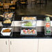 A large chrome American Metalcraft three-tier display stand holding bowls of snacks and a tray of muffins on a counter.