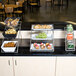 A American Metalcraft chrome display stand with three tiers holding bowls of snacks on a counter.