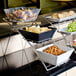 A medium chrome three-tier display stand with bowls of snacks on a hotel buffet table.