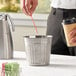 A person holding a straw in a silver mini metal trash can.