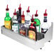 An Advance Tabco stainless steel double tier speed rail holding bottles of alcohol on a counter.