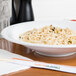A CAC super bright white porcelain bowl filled with noodles and chopsticks on a table.
