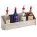 A stainless steel Advance Tabco speed rail holding three bottles of liquor and a bottle opener on a counter.