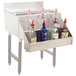 A silver bar with a stainless steel Advance Tabco speed rail holding bottles of alcohol.