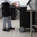 A chef pushing a black Carlisle mobile ice bin with wheels.