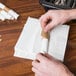 A hand holding a Natural Kraft paper napkin band with white napkins inside.